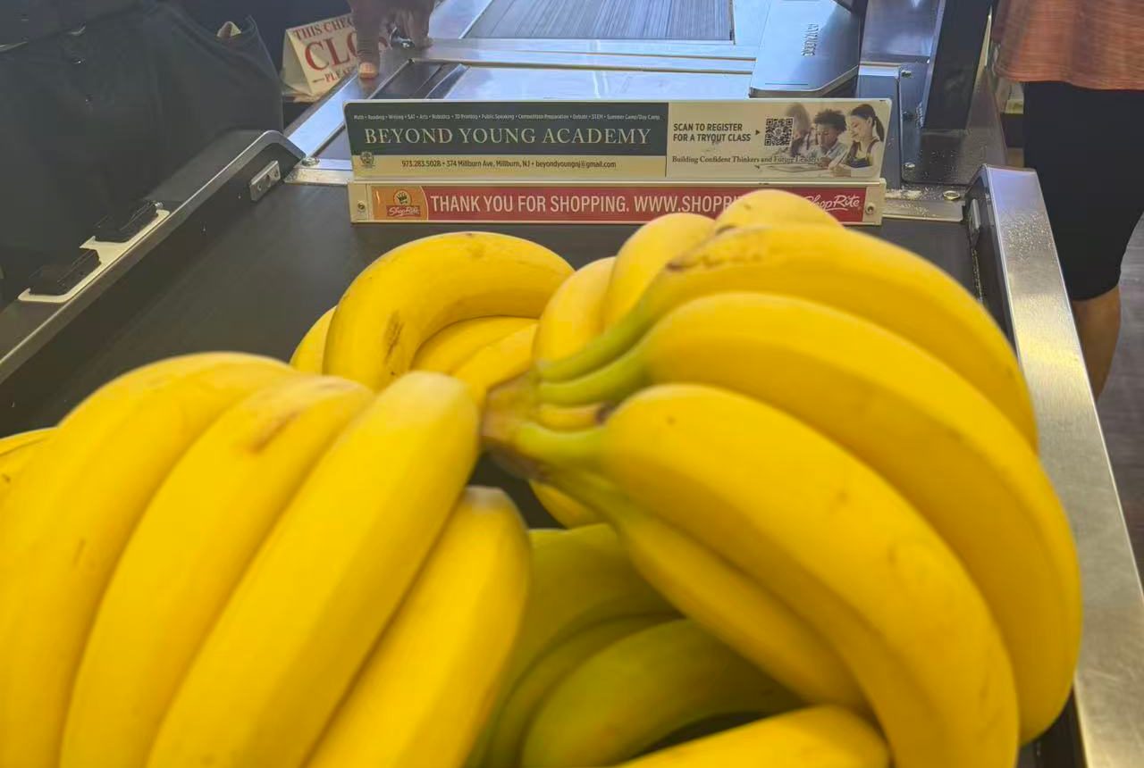 Bananas on the ShopRite checkout belt, with the Beyond Young Academy sign on the lane divider behind them